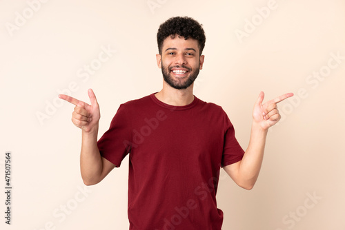 Young Moroccan man isolated on beige background pointing finger to the laterals and happy