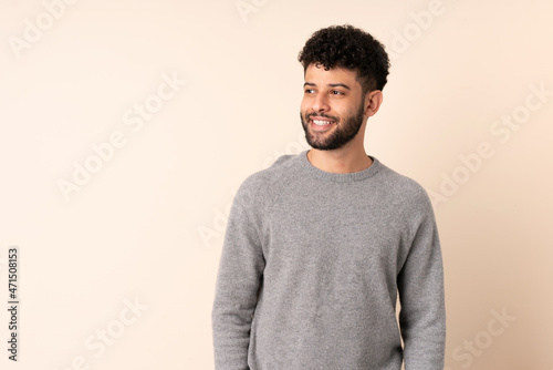 Young Moroccan man isolated on beige background looking to the side and smiling