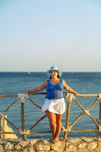 Young brunette woman in a white skirt and blue hat on the seashore happy. © finist_4