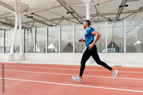 Fit man with sportswear and sunglasses running on the field track photo