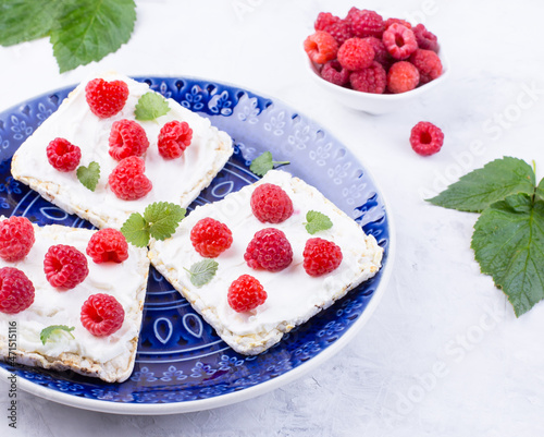 Toast with cream cheese and fresh raspberries on a blue plate. A delicious summer dish for breakfast.