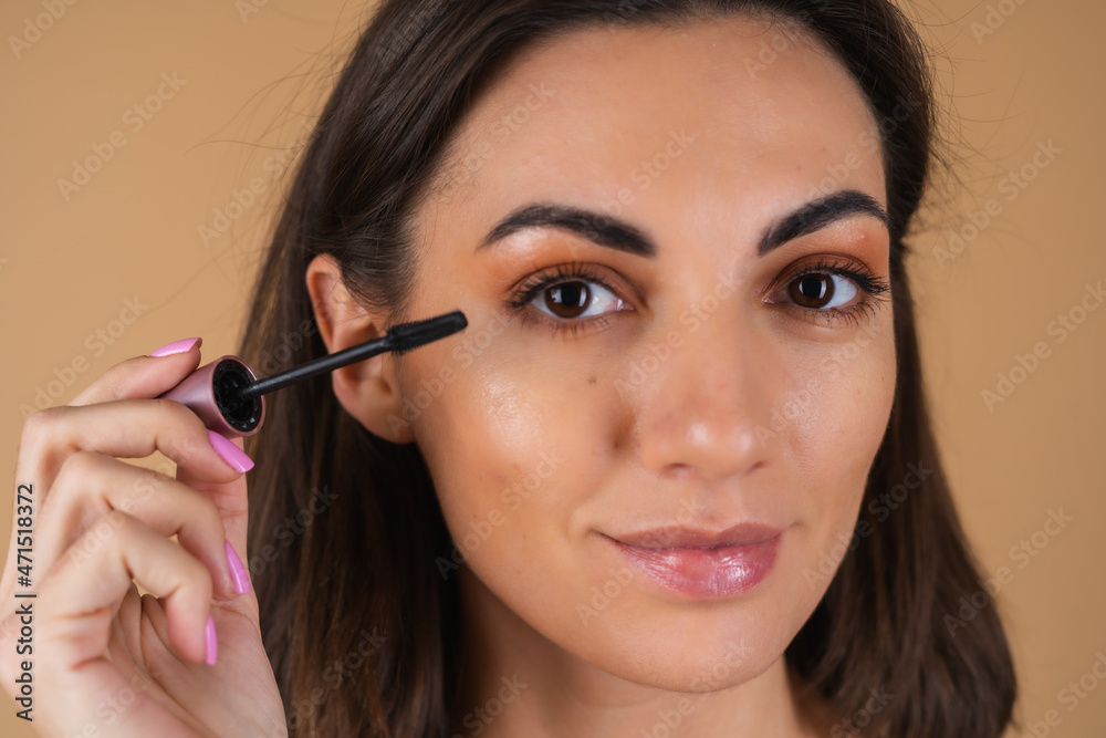 Portrait of a young woman on a beige background with natural warm make-up and smooth clean skin, holding mascara Portrait of a young woman on a beige background with natural warm make-up and smooth clean skin, holding mascara