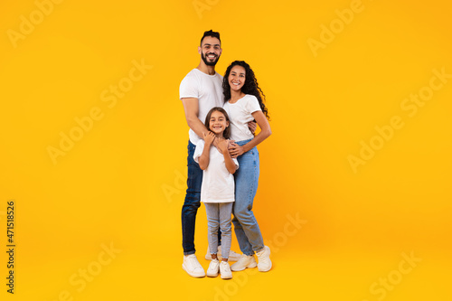 Full-Length Shot Of Middle-Eastern Family Hugging Standing On Yellow Background