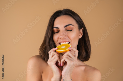 Portrait of a young woman on a beige background with natural warm make-up and smooth clean skin, holding orange circles