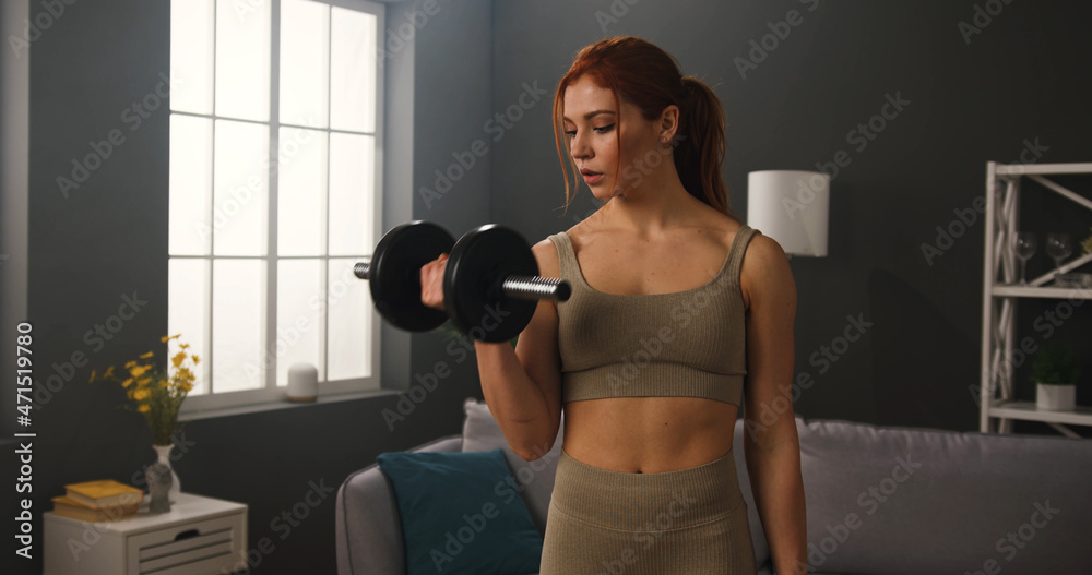 Fit muscular woman working out at home, doing power and strength exercises, using dumbbells. Healthy lifestyle concept.