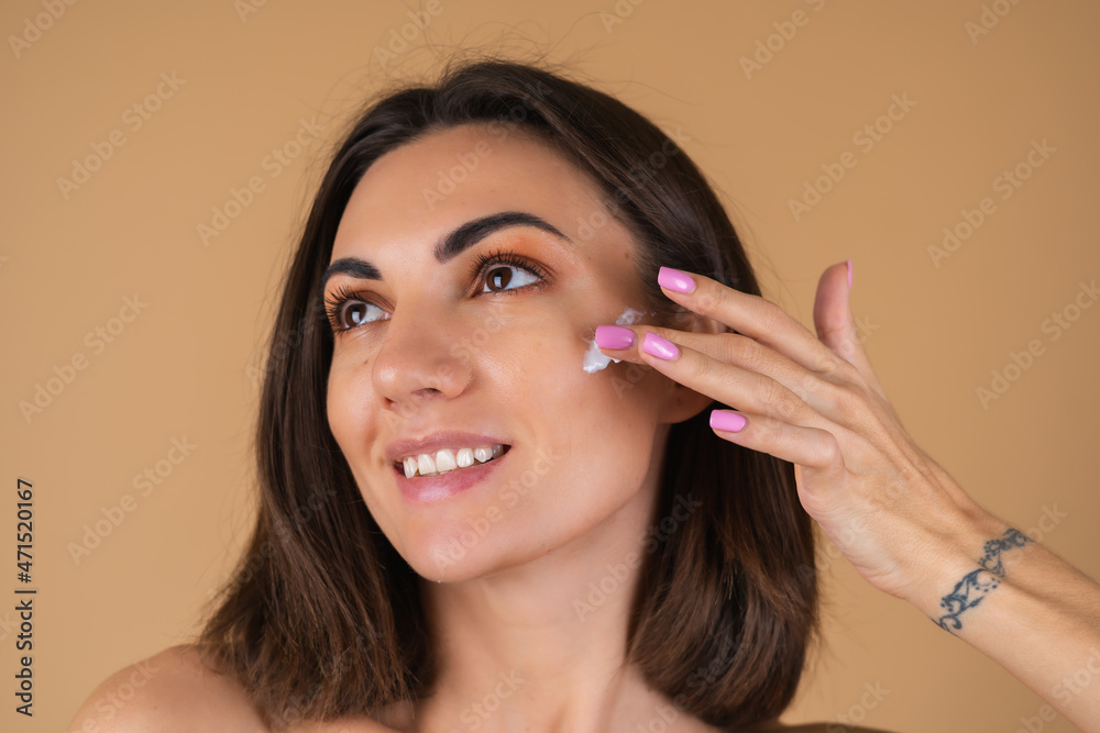 Portrait of a young woman on a beige background with natural warm make-up and smooth clean skin, applies cream on her face Portrait of a young woman on a beige background with natural warm make-up and smooth clean skin, applies cream on her face