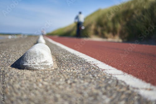 Fototapeta Naklejka Na Ścianę i Meble -  Bicycle path in South Holland. 1 man in dark clothes on bike deep out of focus. Large beach dune with grass. Deep perspective on a day in summer. Netherlands, Schouwen-Duiveland, Brouwersdam.