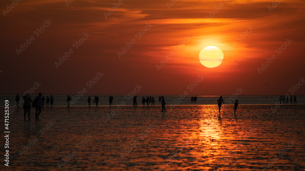 A group of people on the beach in the reflektion of the sunset off Buesum in the Wadden Sea.