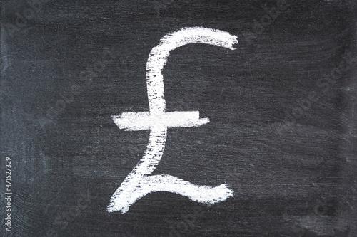 The symbol of the pound sterling on a black chalk board drawn in white chalk. Close up