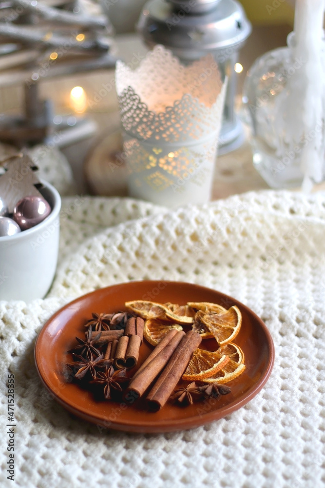 Plate with cinnamon, anise and dry oranges, cozy blanket, various Christmas deocrations and lit candles. Hygge at home. Selective focus. Plate with cinnamon, anise and dry oranges, cozy blanket, various Christmas deocrations and lit candles. Hygge at home. Selective focus.