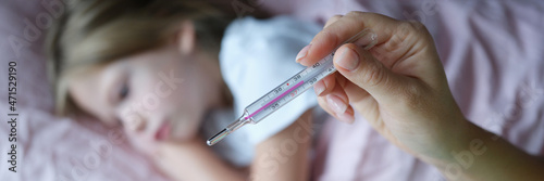 Woman hand holding mercury thermometer with high temperature on background of child sick with flu closeup