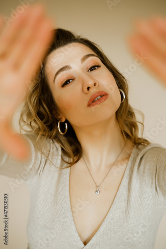young caucaisan woman extends her arms out in front of her, beauty girl looks forward and puts her palms out, portrait of a young european lady at the beige wall, who puts her hands out in front of