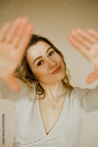 young caucaisan woman extends her arms out in front of her, beauty girl looks forward and puts her palms out, portrait of a young european lady at the beige wall, who puts her hands out in front of