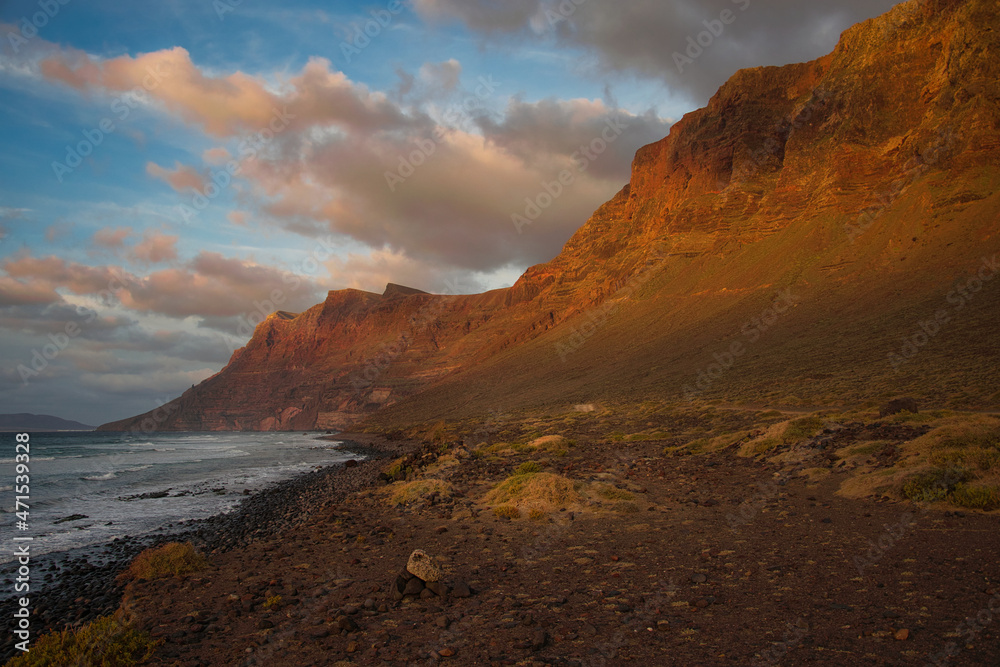 A beautiful sunset at the cliffs near Famara Beach, Lanzarote, Spain. Some clouds in a blue sky. The last sunlight is shining on the mountain tops.