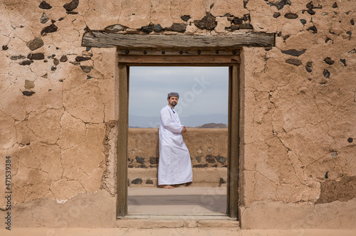 omani man in traditional outfit at a doorway of an old house © SELIMBT