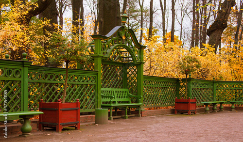 a beautiful green fence in the park. benches near the fence. bushes with yellow leaves. autumn park