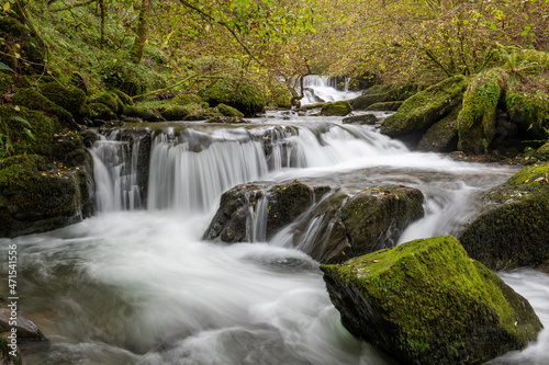 Fototapeta Naklejka Na Ścianę i Meble -  Long exposure of a waterfall flowing through the woods at Watersmeet in Exmoor National Park