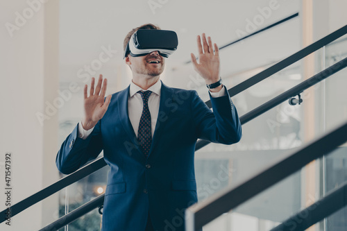 Young excited europian businessman in formal wear standing in office interior using VR headset photo