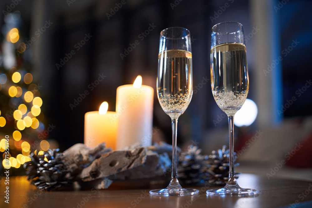 Two glasses of champagne standing on table with christmas tree on background. Candles as decoration around. Concept of winter holidays. Two glasses of champagne standing on table with christmas tree on background. Candles as decoration around. Concept of winter holidays.
