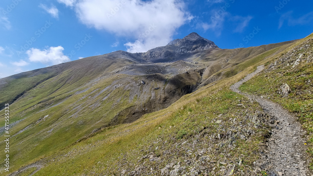 A panoramic hiking trail leading to the Chaukhi Pass in the Greater Caucasus Mountain Range in Georgia, Kazbegi Region. Clouds are covering the mountain summit. Wanderlust. Remote location.