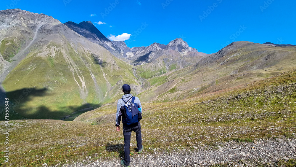 A man watching the sharp mountain peaks of the Chaukhi massif form the Chaukhi Pass in the Greater Caucasus Mountain Range in Georgia, Kazbegi Region. The female backpacker enjoys the calmness. Hike