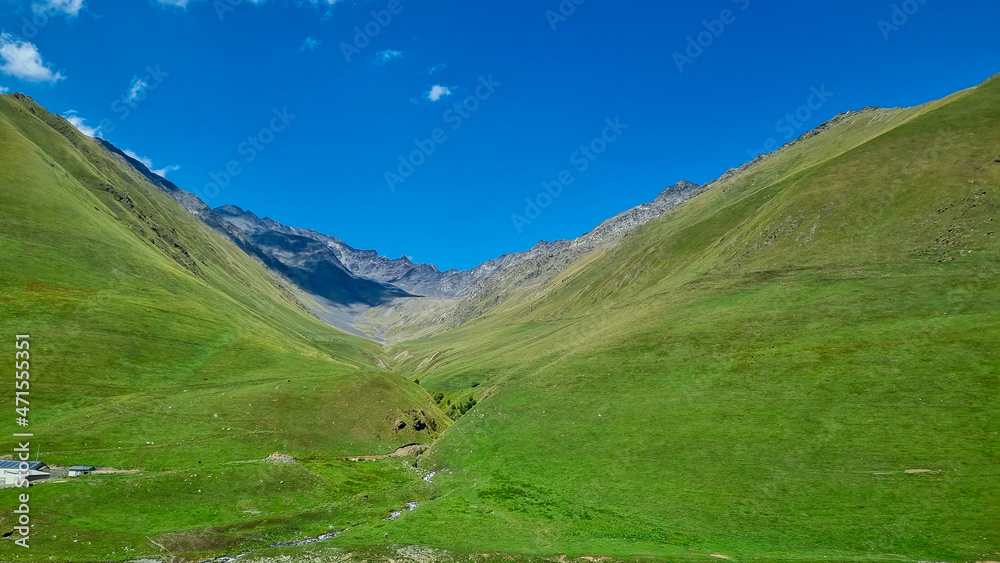 A  green grassland in the Greater Caucasus Mountain Range in Georgia, Kazbegi Region. The surrounding mountains and hills are green and soft. Tranquility. Highlands. Clear Sky.
