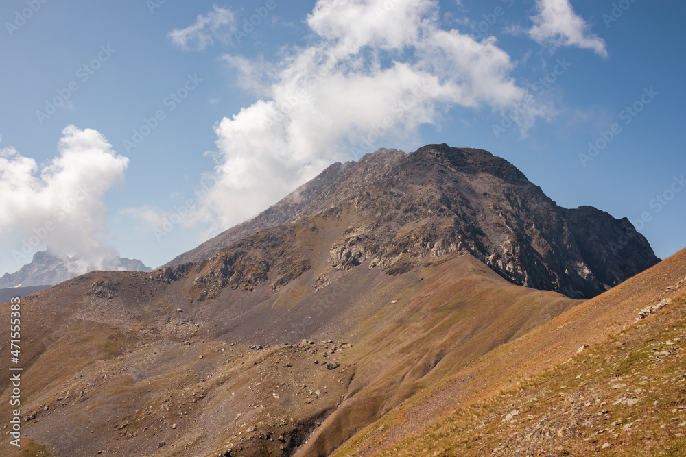 A panoramic view on the sharp mountain peaks of the Chaukhi massif in the Greater Caucasus Mountain Range in Georgia, Kazbegi Region. Clouds emerging over the Chaukhi Pass. Georgian Dolomites. Hike