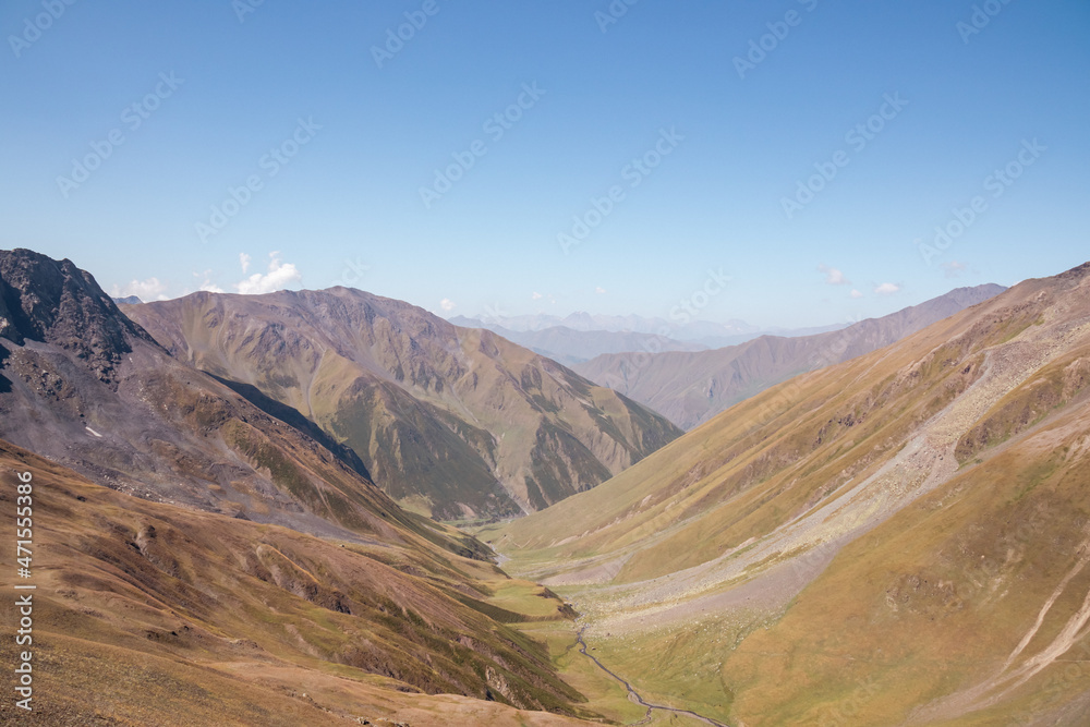 Panoramic view on a alpine terrain seen from the Chaukhi Pass in the Greater Caucasus Mountain Range in Georgia, Kazbegi Region. A small river flows through the valley. Hiking Trail Juta-Roshka.
