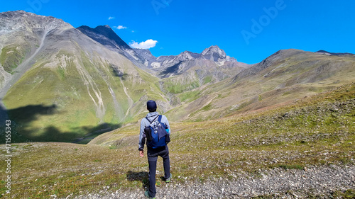 A man watching the sharp mountain peaks of the Chaukhi massif form the Chaukhi Pass in the Greater Caucasus Mountain Range in Georgia  Kazbegi Region. The female backpacker enjoys the calmness. Hike