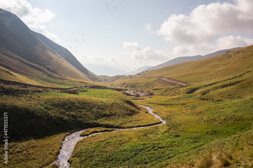 A panoramic view on the Kmosti River flowing down a valley near the village in Roshka in the Greater Caucasus Mountain Range in Georgia, Kazbegi Region. Landscape after sunrise, twilight. Wanderlust. photo