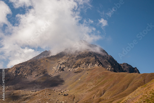 A panoramic view on the sharp mountain peaks of the Chaukhi massif in the Greater Caucasus Mountain Range in Georgia, Kazbegi Region. Clouds emerging over the Chaukhi Pass. Georgian Dolomites. Hike