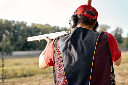 Rear view on caucasian Man in cap and headphones shooting at target on an outdoor shooting range at sunny day, training alone, confident and skilled, experienced. Shooting and guns. view from back.