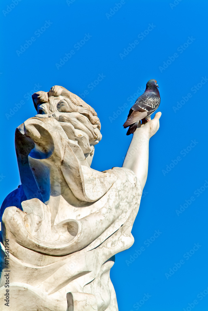 back view, medium distance of statue of a woman holding hand toward blue sky with a pigeon perched in the palm