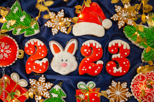 Banner for Christmas and New Year gingerbread cookies numbers 2023, snowflakes, Santa hat, Christmas trees, garlands on blue silk fabric background, gingerbread rabbit symbol Chinese zodiac calendar