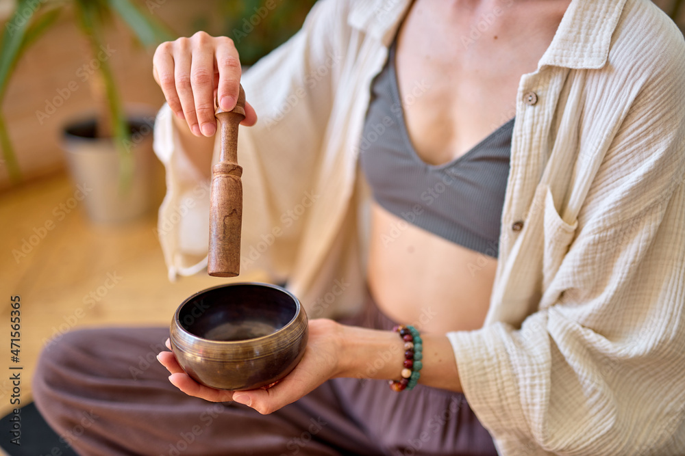 Woman using singing bowl in sound healing therapy at home, sitting alone at home, unrecognizable female in domestic wear pajamas begins morning with yoga practice, sit relaxed. Close-up photo of hands Woman using singing bowl in sound healing therapy at home, sitting alone at home, unrecognizable female in domestic wear pajamas begins morning with yoga practice, sit relaxed. Close-up photo of hands