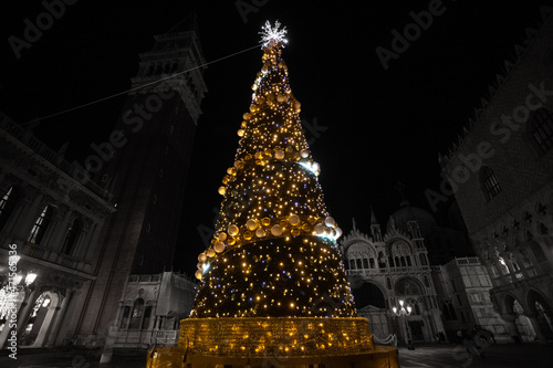 Christmas tree with lights and gold colored balls. Black and white background of San Marco square in Venice. Theme concerning the symbols of Christmas