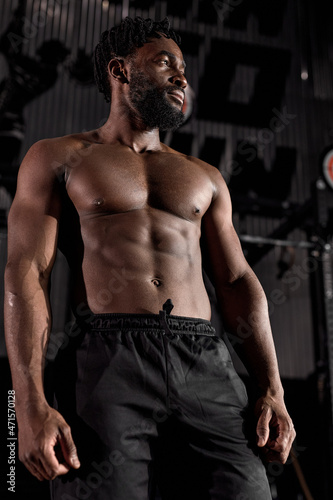 Portrait of serious muscular male with naked torso posing standing after workout in gym, looking confident and motivated. handsome guy with beard wearing black shorts looking at side