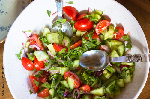 Vegetable salad of fresh herbs, sliced tomatoes, tomatoes, cucumbers, seasoned with natural olive oil in a white deep bowl bowl view above. A healthy dietary homemade meal flatly. Rural simple food.