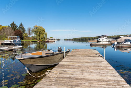Fototapeta Naklejka Na Ścianę i Meble -  Motorboat moored to a weathered wooden jetty in a river harbour on a clear autumn day. Tranquil scene.