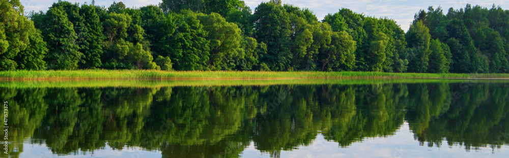 Panoramic view of the lake in summer. Reflection of green trees and clouds in the water Panoramic view of the lake in summer. Reflection of green trees and clouds in the water