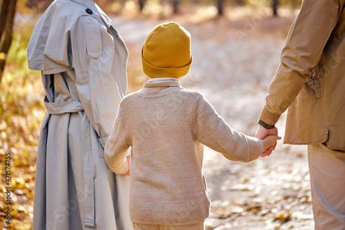 View from back on family with child boy walking having fun in forest on autumn season, caucasian european fmaily in coats enjoy warm weather outdoors. human emotions, lifestyle, childhood, family photo