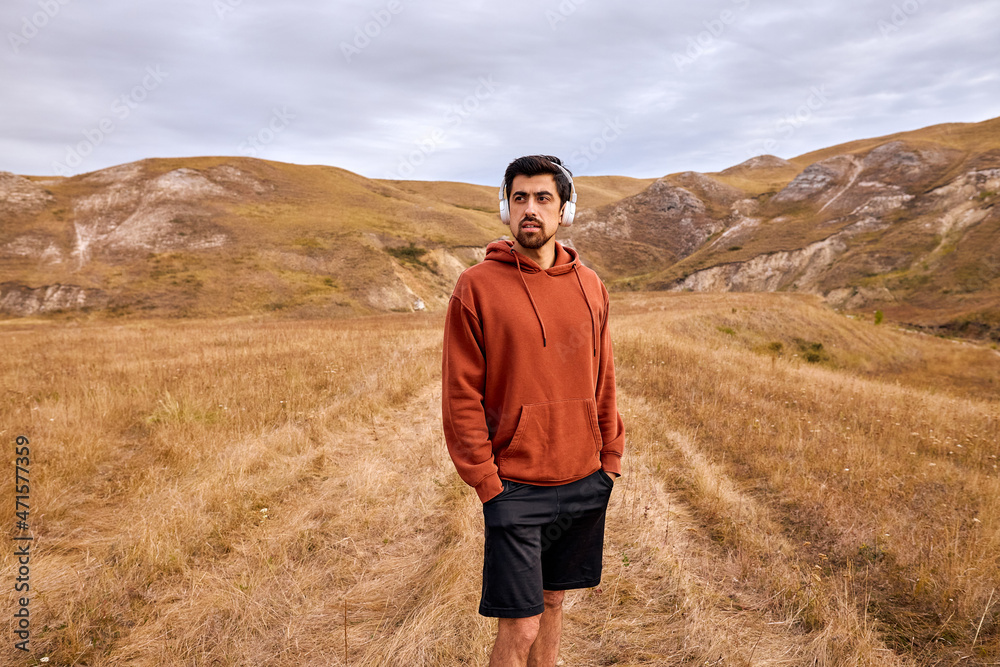 Naklejka premium Thoughtful Calm Man Listen To Music, Walking Alone In Field In countryside at summer or autumn season. fit caucasian male thinking about life, having rest far from civilization, city