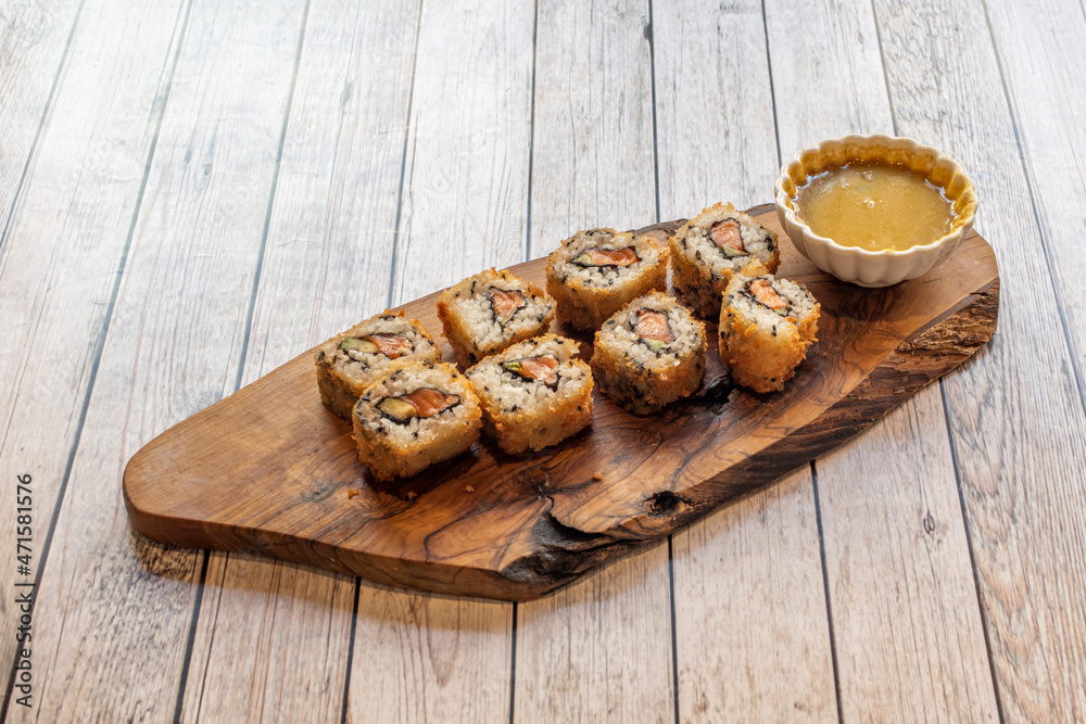 Crispy fried uramaki roll sushi with salmon and nori seaweed and curry sauce for dipping on wooden plate Crispy fried uramaki roll sushi with salmon and nori seaweed and curry sauce for dipping on wooden plate
