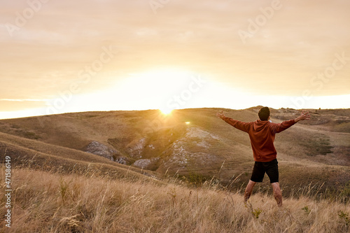 excited unrecognizable man stands against the backdrop of mountain landscape with hands raised high In the morning at sunrise time. Autumn, Summer, sun, dawn. Human emotions. View from back