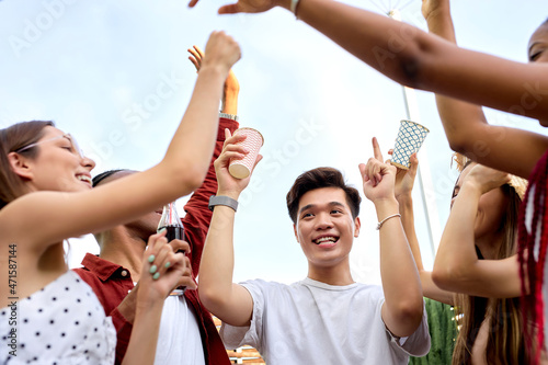 group of excited students, young diverse men and women at party in nature, raising hands with beverages, celebrating the end of exams, have fun at picnic, summer time concept, friendship