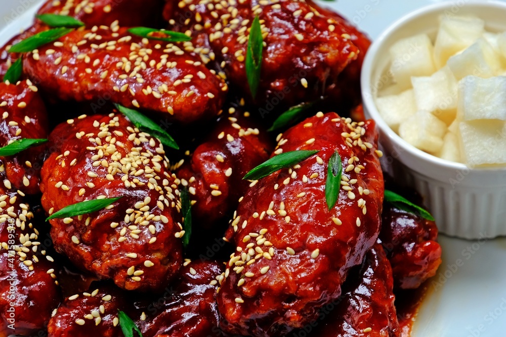 Crispy and crunchy Korean fried chicken wings (Dakgangjeong) in white plate on wooden table. Crispy and crunchy Korean fried chicken wings (Dakgangjeong) in white plate on wooden table.