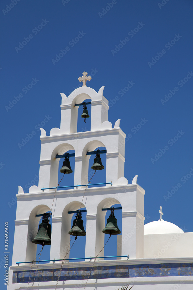 Traditional Greek white church with cross and bells in village Oia on Santorini, Greece. Oia is a small town and former community in the South Aegean on the islands of Santorini.