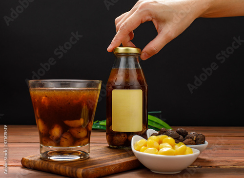 Hand picking up juice bottle from meal table of natural organic beverage, drink glass, bowl of sweet ginkgo, preserved Malva nut photo