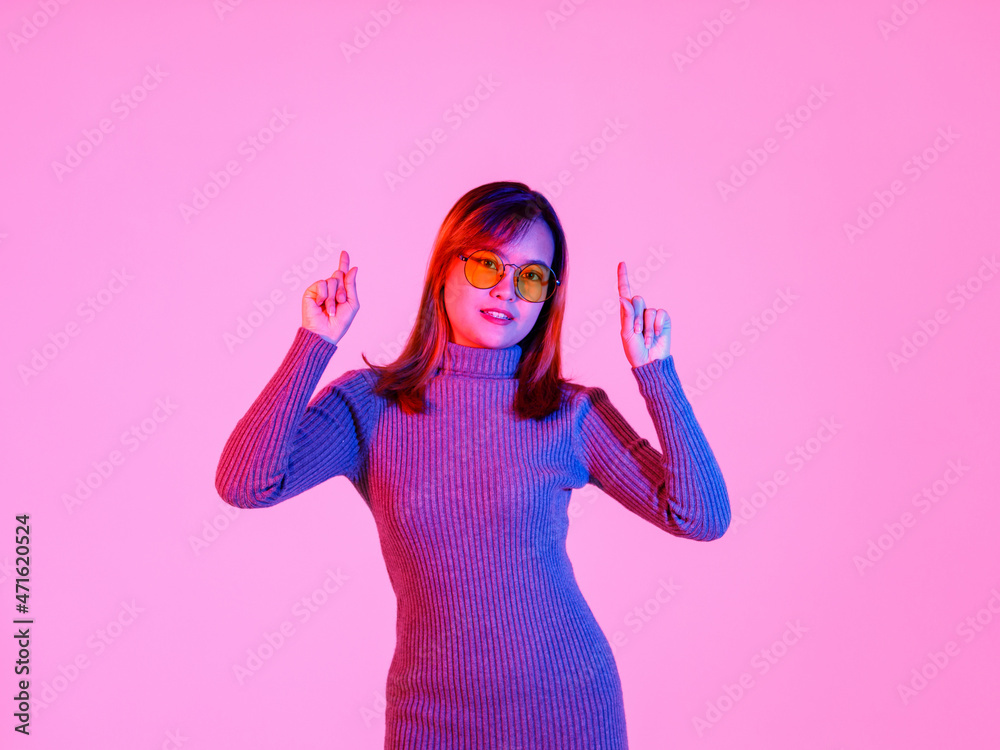 Studio shot Asian young female model in gray turtleneck sweater and orange lens sunglasses standing pointing index fingers to empty copy space presenting promoting product on pink light background Studio shot Asian young female model in gray turtleneck sweater and orange lens sunglasses standing pointing index fingers to empty copy space presenting promoting product on pink light background
