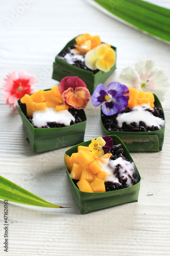 Homemade Coconut Black Sticky Rice with Mango in Pandan Leaves Cup, Selective Focus with Pansies Edibel Flower Topping photo